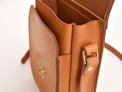 職人手作皮革翻蓋迷你單肩包 (CP-6)，採用光滑的棕色皮革製成，配有黃銅色金屬扣環和可調節的皮革肩帶。包包設計簡約，展現天然皮革紋理，適合日常搭配。