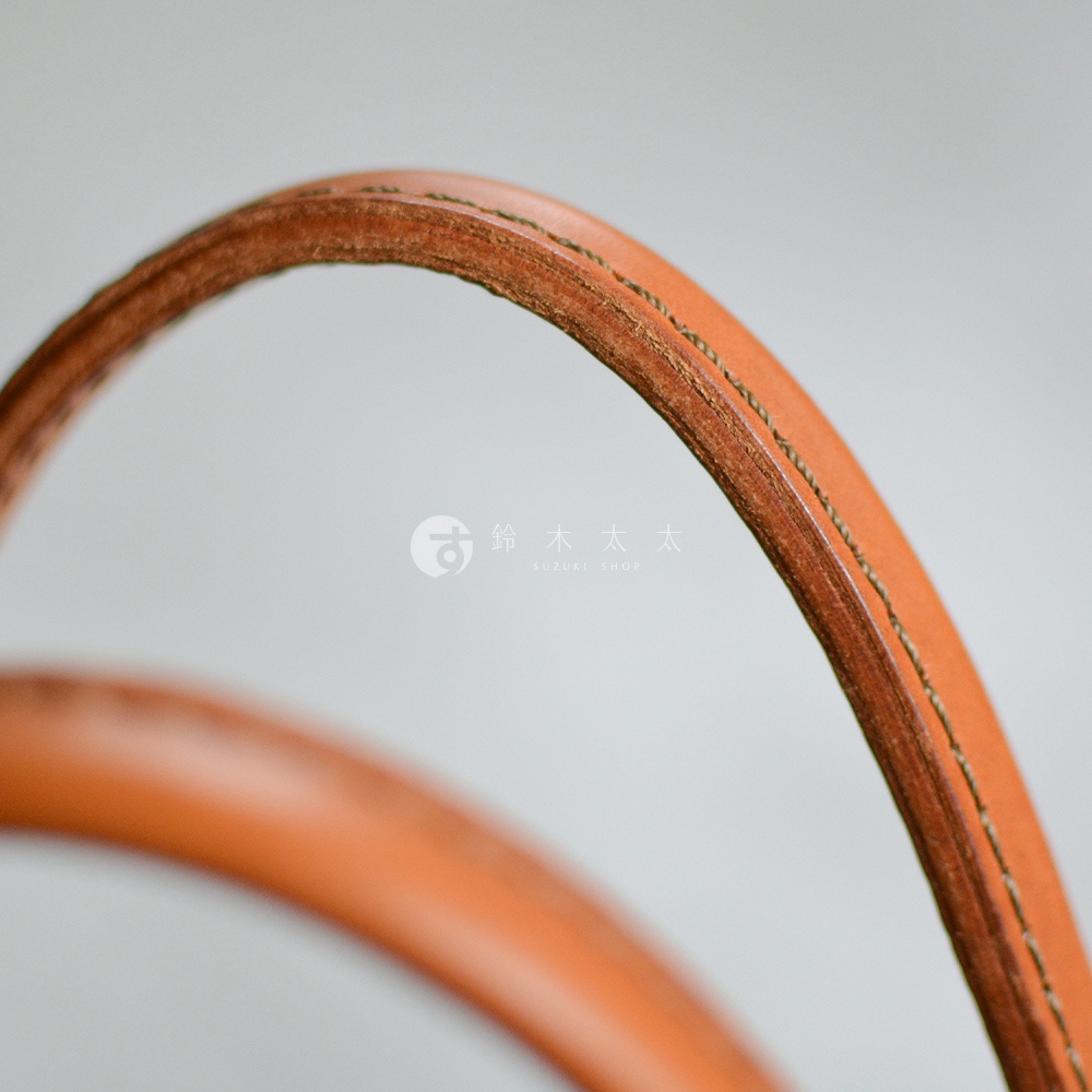 特寫鏡頭展示了棕褐色皮革提把的縫線細節，背景為淺灰色。