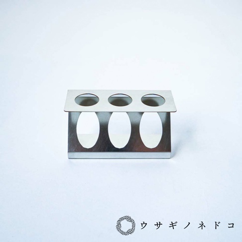 銀色金屬製試管架，可容納三個試管，頂部有三個圓形開口，下方有三個橢圓形開口。