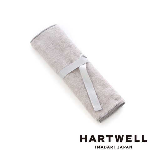 淺灰色毛巾材質的牙刷收納袋，捲起後用淺灰色織帶束緊，兩端有灰色滾邊，整體簡潔實用。