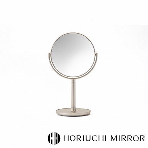 香檳金色的圓形桌上化妝鏡，鏡框為金屬材質，鏡面可旋轉，底部有圓形底座，整體設計簡潔。