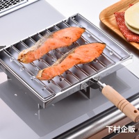 銀色金屬燒烤盤上放著兩塊烤鮭魚，燒烤盤有木製手柄，置於瓦斯爐上。