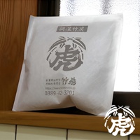 中型孟宗竹炭包，白色紙質包裝，印有灰色「虎」字圖案及日文標示，置於木質檯面上。