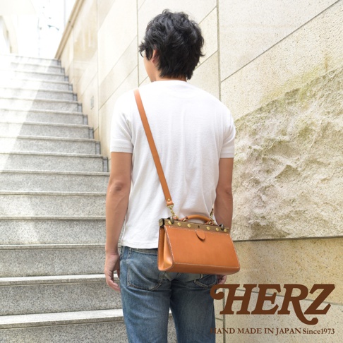 職人手作皮革復古口金兩用手提包，皮革材質，顏色為自然的棕褐色。包款設計簡潔，帶有復古金屬口金和提把，並配有可拆卸的長肩帶，可側背或手提。