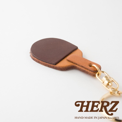 職人手作皮革桌球拍造型鑰匙圈，由兩種不同色澤的皮革製成，拍面為深棕色，拍柄為淺棕色，搭配金色金屬扣環。