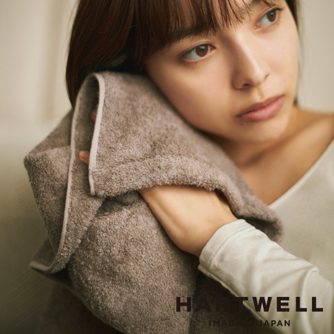 一名女子正在用一條淺棕色的毛巾擦拭頭髮。毛巾質地柔軟，邊緣有細緻的滾邊。
