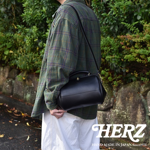 黑色皮革口金醫生單肩包，附有提把和可調式斜背帶。包身結構飽滿，線條簡潔，採用傳統縫線工藝，展現皮革質感。