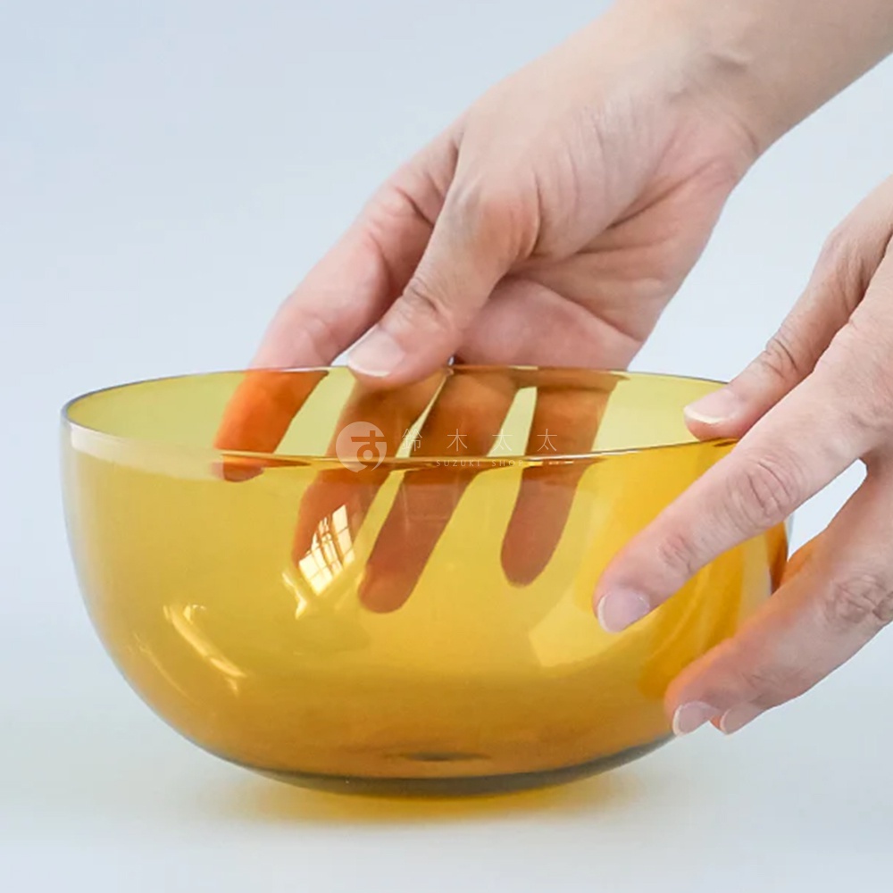 琥珀色玻璃製成的圓潤點心碗，碗壁光滑，可見碗內黃色燈光照射下的手指輪廓。