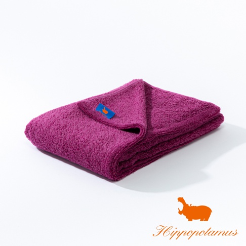一張紫紅色竹棉混紡厚感大浴巾，整齊對折，左上角縫有藍色標籤，上面印有橘色河馬圖案。