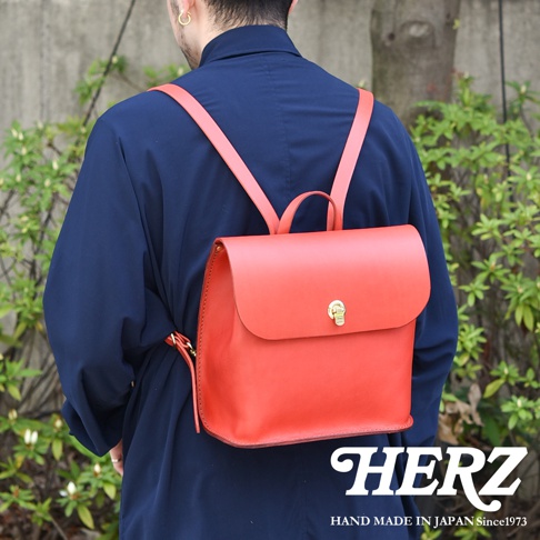 職人手作皮革翻蓋迷你後背包，採用亮紅色皮革，配有金色旋轉鎖扣和可調式肩帶。