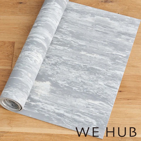 WE HUB 品牌標誌下的灰色大理石紋路瑜珈墊，部分展開鋪設在木地板上