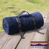 深藍色絨面睡袋毯捲起，以黑色織帶和卡扣固定，方便攜帶，置於戶外的木桌上。