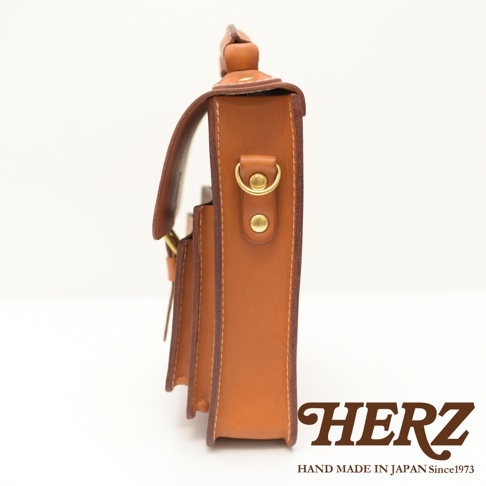 職人手作棕色皮革單肩兩用小方包，側邊視角，展示精緻車縫線、黃銅金屬扣環與鈕扣。