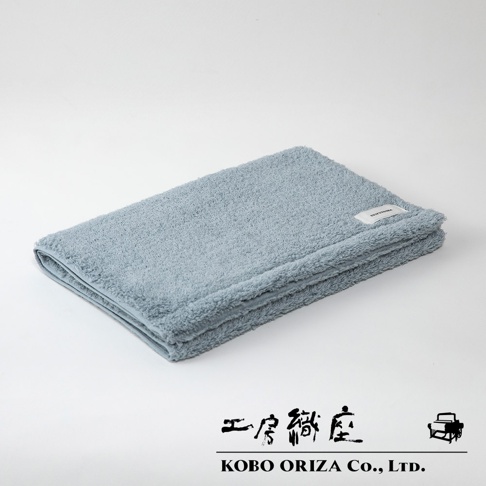 一條淺藍色的今治匹馬棉毛巾，質地柔軟，表面有細緻的絨毛，毛巾上縫有一個白色的小標籤。