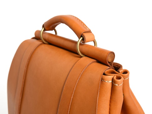 職人手作皮革屋瓦風經典雙扣後背包 (R-153)，採用溫暖的棕褐色皮革，搭配金屬扣環，展現經典設計與細膩工藝。