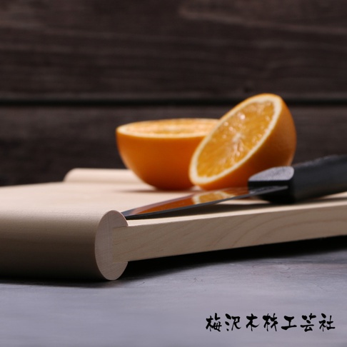 淺色木質砧板上放著對半切開的橘子和一把黑色手柄的刀，砧板右側邊緣圓潤，木紋清晰可見。