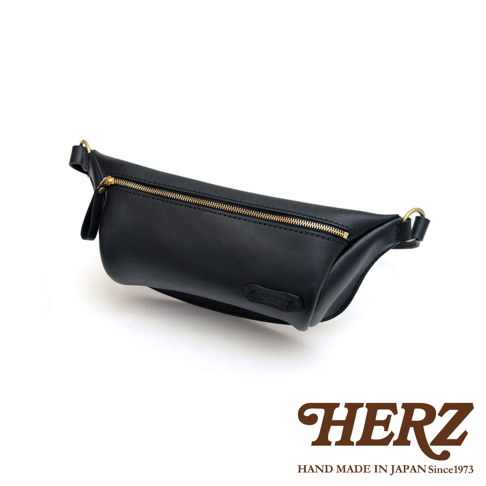 黑色職人手作皮革輕便斜背包，設有金色拉鍊及扣環，簡約實用。