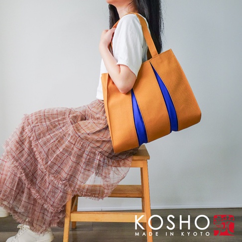 芥黃色棉帆布扇形托特包，飾有兩條鮮豔的皇家藍色飾帶，搭配同色系提把，造型簡潔大方，為日常穿搭增添亮點。