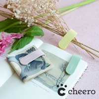 粉色、淺綠色和黃色的萬能QQ變形夾，夾在日圓紙鈔和書本上，背景為乾燥花束與粉色紋理桌面。