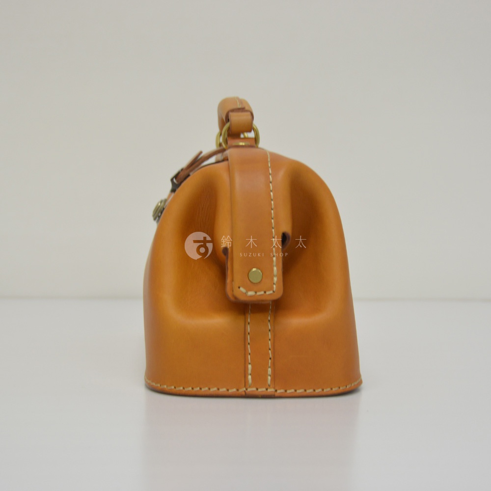 職人手作皮革長型迷你醫生包，淺棕色皮革，圓潤包身，頂部有提把和金屬扣環，包身縫線整齊，風格經典。