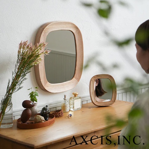掛在牆上的橢圓形木框鏡子，鏡框為淺木色，表面光滑。旁邊的木質桌面上擺放著一束乾燥花、香水瓶、小裝飾品，以及另一面小巧的木框鏡子。