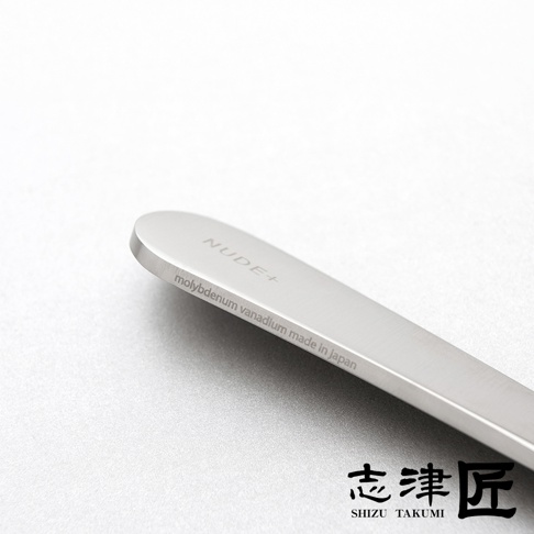 一個金屬削皮刀，上面刻有「NUDE+」和「molybdenum vanadium made in Japan」的字樣，下方有「志津匠 SHIZU TAKUMI」的品牌標識。