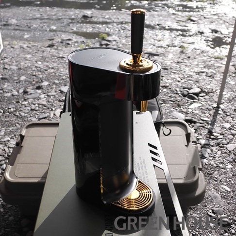 GREEN HOUSE 超音波四代金泡機 GH-BEERT-BK，具有黑色機身與金色觸控面板，放置於戶外環境的桌面上，背景為河邊的礫石與流水。