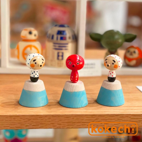 三款木芥子開運擺飾，分別為紅色章魚造型與兩款白色頭巾、圓點圖案人偶，皆立於藍白相間的富士山造型木座上。