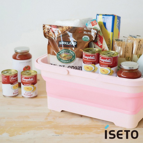粉色與白色相間的伸縮提籃，籃中裝有Kirkland品牌穀物、Campbell's玉米濃湯罐頭、番茄醬罐及其他食品雜貨。