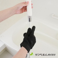 一隻黑色編織材質的萬用清潔手套，戴在手上，正握著一根白色帶有銀色金屬接頭的清潔工具，背景是白色浴缸。