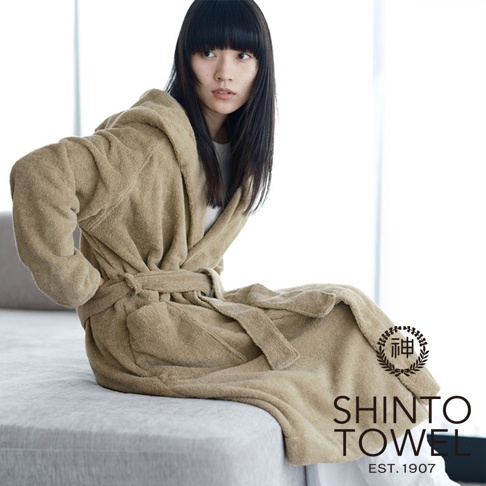 身穿米色蓬厚長袖連帽浴袍的女子，浴袍以腰帶繫住，材質柔軟，整體呈現舒適感。