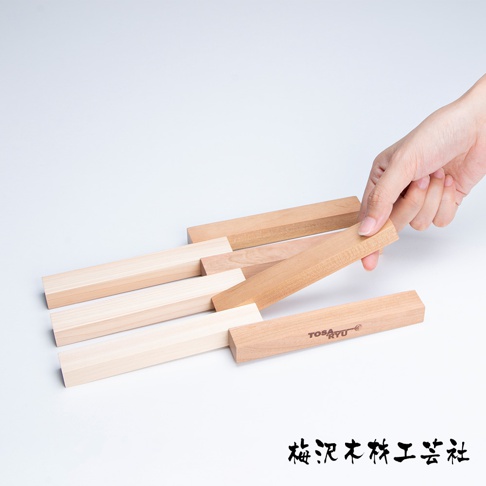 數根淺木色和深木色的長條形木製隔熱墊，整齊排列，其中一根由手輕輕拿起，上面印有「TOSARYU」字樣。