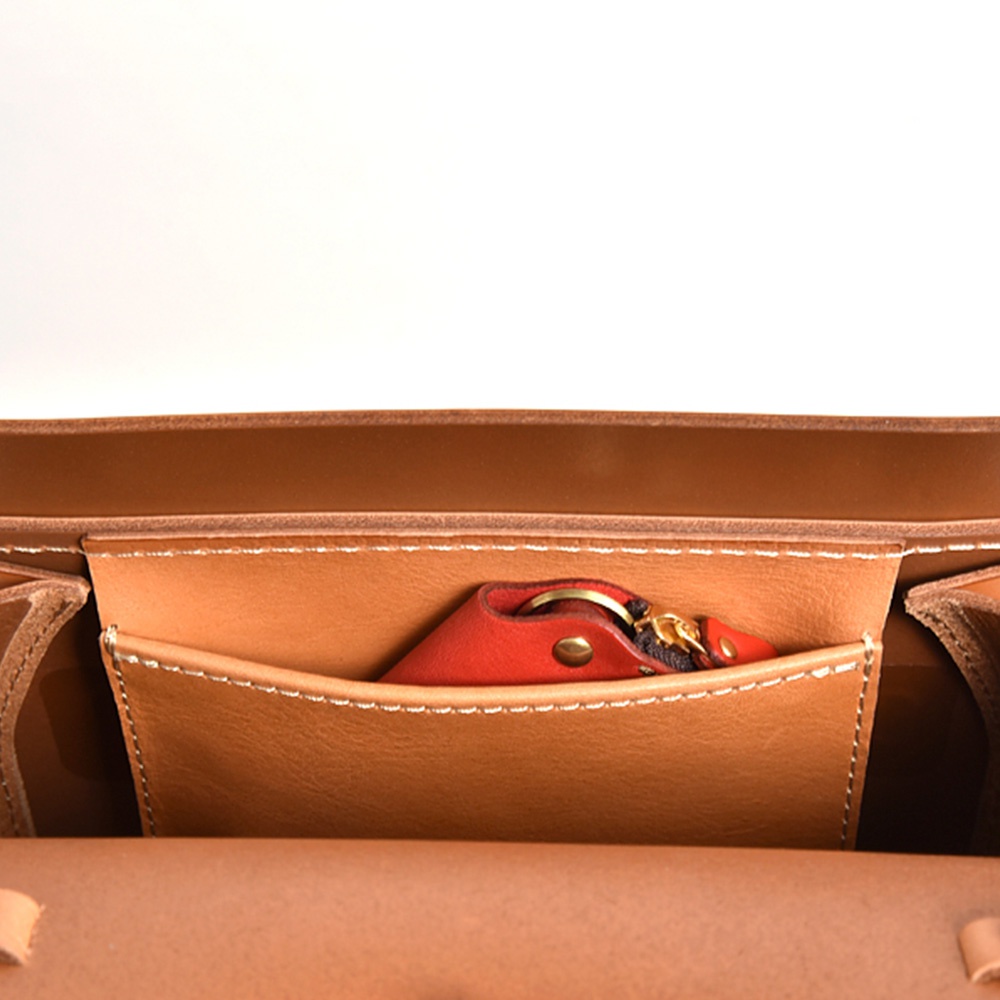 職人手作皮革後背包 R-31 (厚實版)，展示包款內部，焦糖色皮革外觀，有一個紅色皮革鑰匙包，置於前袋中，搭配縫線細節。