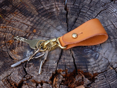 淺棕色皮革鑰匙圈，配有黃銅色登山扣和鑰匙環，上面掛有幾把銀色鑰匙，放置在有紋理的木頭背景上。