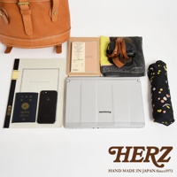 棕色皮革後背包、日本護照、黑色手機、筆記本、2019年曆、相機、毛巾、銀色筆記型電腦和黑色印花雨傘，擺放在白色背景上。