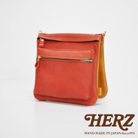 橘紅色皮革翻轉雙色直式斜背包，正面有拉鍊口袋，採用金屬拉鍊，皮革材質，純手工製作。