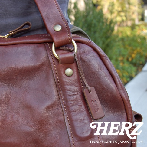 職人手作皮革水洗加工迷你波士頓包，呈現深棕色皮革紋理，搭配黃銅色五金配件，包包上有品牌壓印小皮標。