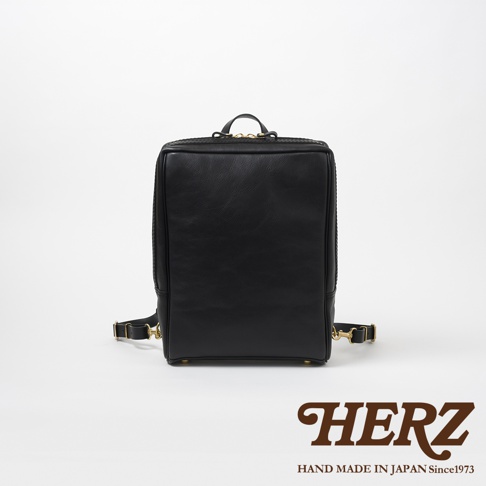 黑色皮革方形商務後背包，設有金色拉鍊和可調節肩帶，側面有編織紋理。