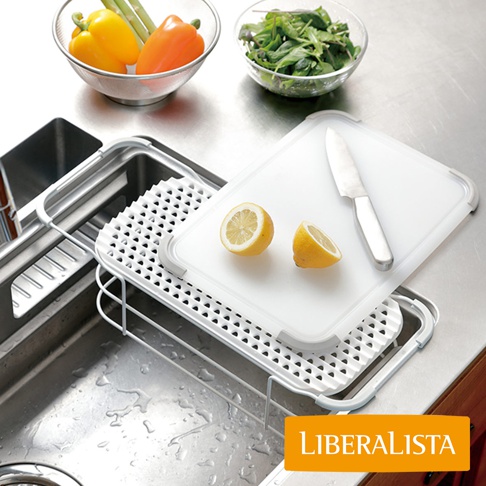 LIBERALISTA 品牌的水槽多功能瀝水籃架，上面放置著兩個半顆檸檬、一把刀，並有一塊瀝水架放在水槽上方，旁邊還放著裝有蔬菜和彩椒的碗。