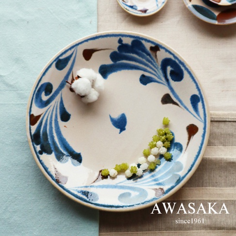 一個白釉陶瓷料理盤，盤面繪有藍色與棕色的植物紋飾，盤中置放著一團棉花和少量白色、綠色糖珠。