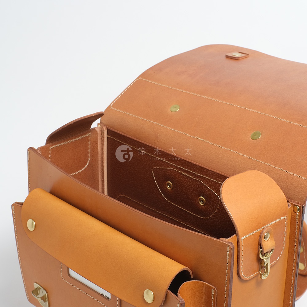 這是一個職人手作的橫式皮革書包，呈現溫潤的棕褐色，包款結構清晰，內部空間可見，搭配金屬釦件，質感十足。