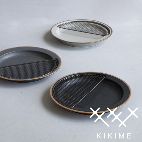 三個美濃燒瀝油餐盤，以灰色與白色為主調，盤緣帶有陶土原色。每個餐盤皆配有半月形黑色金屬濾網，用於瀝除油脂。