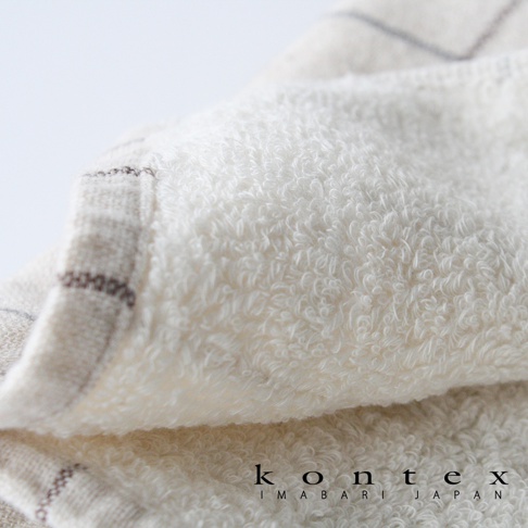 GRAPH 草木染格紋有機棉毛巾，近拍展示其細緻的毛圈織法，呈現天然棉質的蓬鬆觸感。毛巾邊緣處可見以深棕色線條交織的格紋圖案，整體色調為柔和的米白色，質感溫潤。