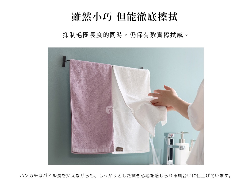 兩條毛巾懸掛在牆上的毛巾架上，一條為粉色，另一條為白色，一隻手正在觸摸白色的毛巾。