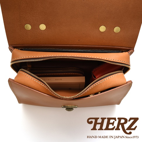 HERZ 職人手作皮革多功能收納單肩包 Q-9，翻蓋打開的內部特寫，可見多層收納空間，一個卡夾與一個紅色的小物包。