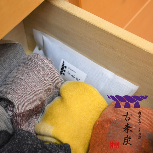 木製抽屜中，幾件捲起的織物，顏色包含灰色、紅棕色、黃色和橙色。其中一件白色包裝的物品上印有日文文字。