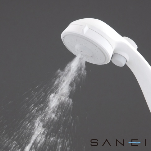 白色塑膠蓮蓬頭，有許多細小的出水孔，正噴射出水流，背景為深灰色。
