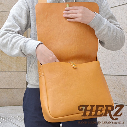 使用日本HERZ職人手作皮革軟皮橫式斜背包，模特兒將手伸入包包內，側邊繡有品牌標誌。