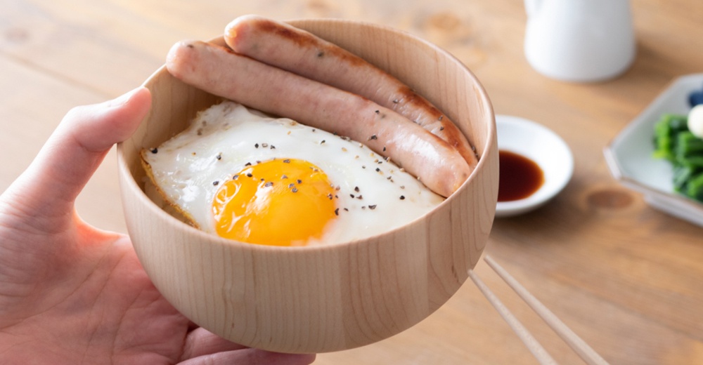 楓木碗裝有飯、太陽蛋和兩條香腸，撒有黑胡椒。