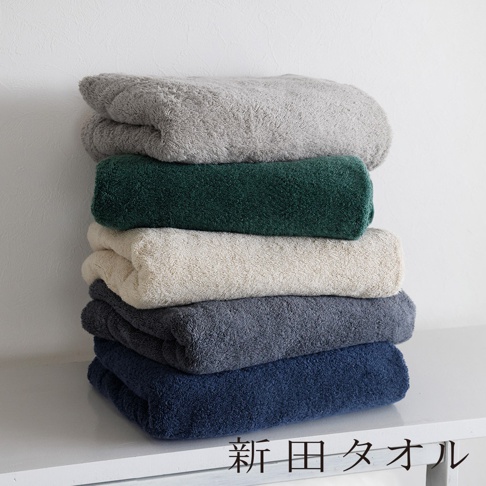 一疊由深藍、炭灰、米白、墨綠與淺灰五種沉穩色系組成的泉州無漿毛巾單人被，層層堆疊於白色平坦檯面上，右下方印有新田タオル文字。